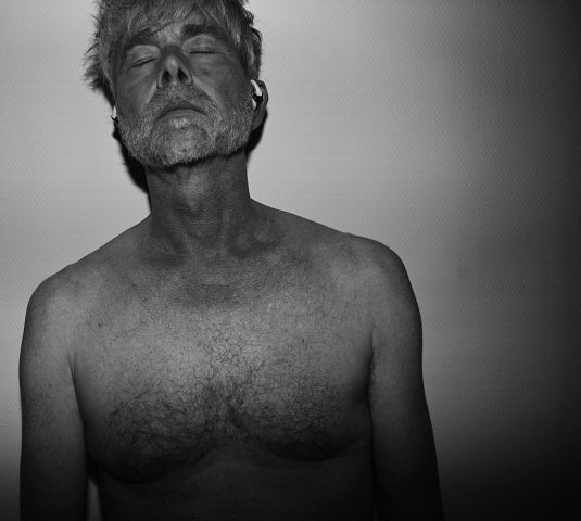 A black-and-white portrait of an older man with his eyes closed and head tilted back, conveying a sense of introspection, tranquility, and vulnerability. The image captures the raw texture of skin and the quiet strength of the moment.