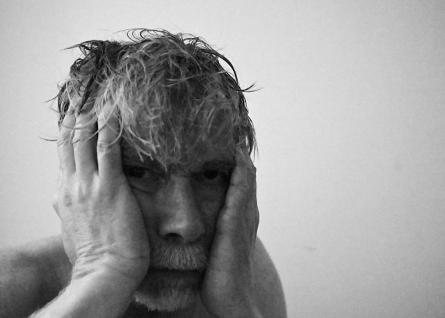 A close-up black and white portrait of a person with their hands in their hair, eyes closed, conveying deep emotion and vulnerability.