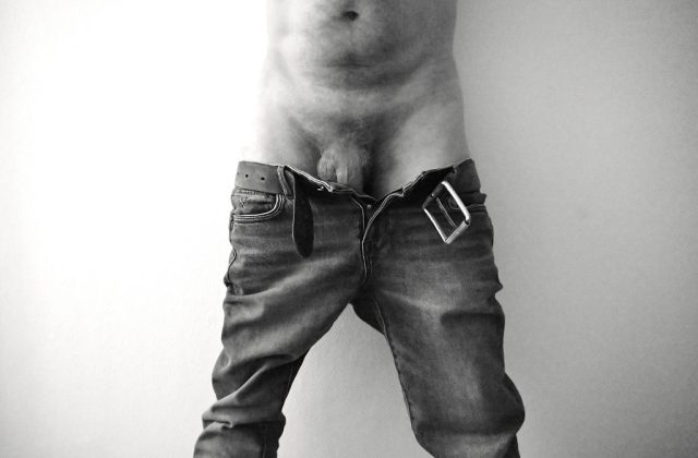 Black-and-white photograph of a person with an unzipped pair of jeans, focusing on the rawness and vulnerability of the moment. The image emphasizes the texture of skin and fabric, radiating a sense of authenticity and unfiltered emotion.